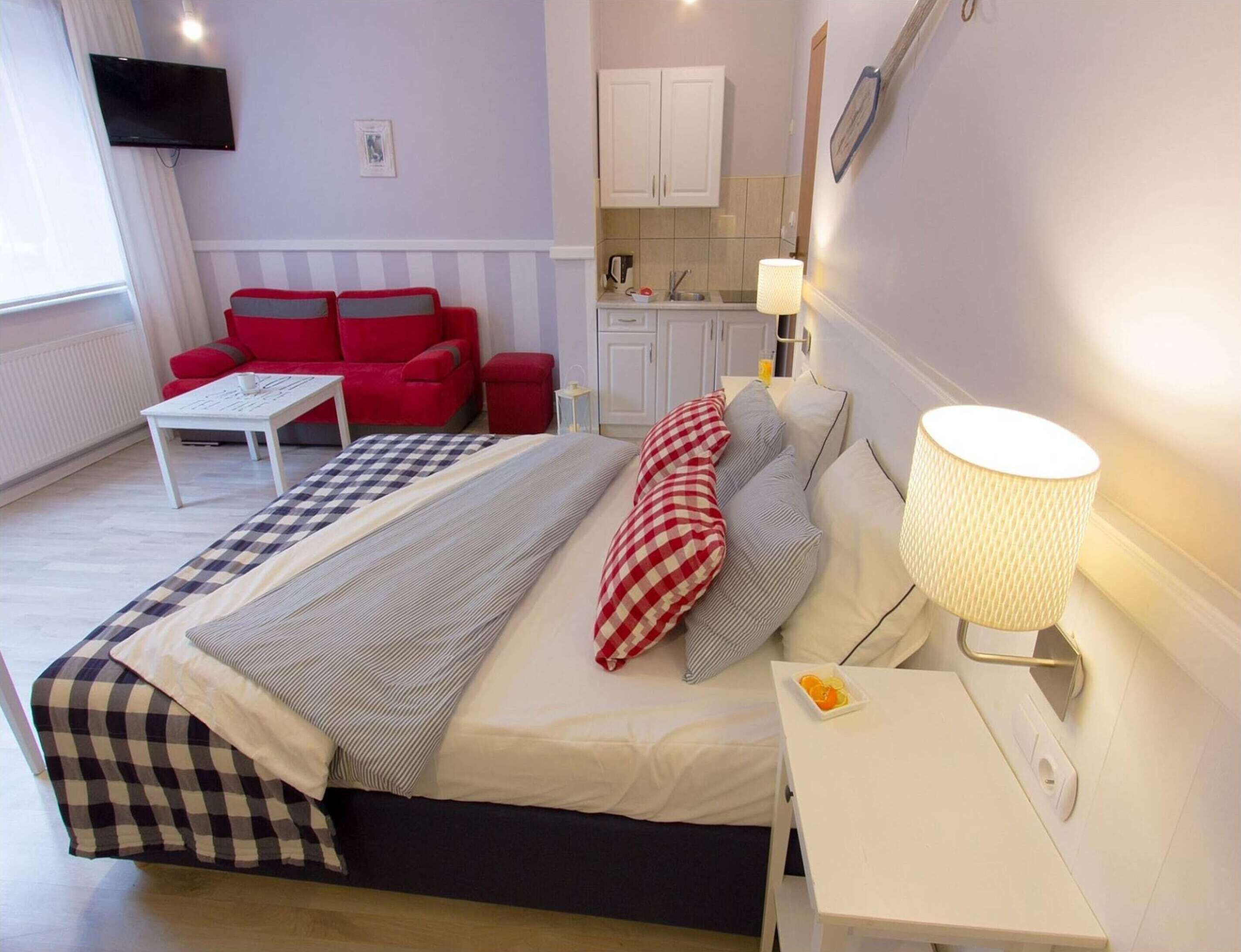 Ett hotellrum med en säng, en röd soffa, ett litet bord, en lampa och ett köksutrymme i bakgrunden.