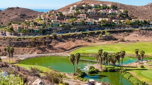 Una zona residencial en una colina con casas modernas, un campo de golf y una masa de agua.