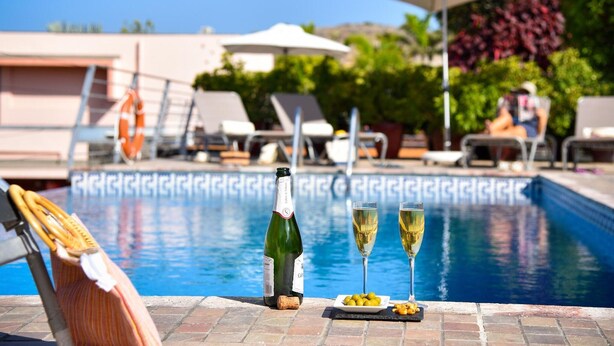 Escena junto a la piscina con una botella de champán, dos copas y un plato de aceitunas.
