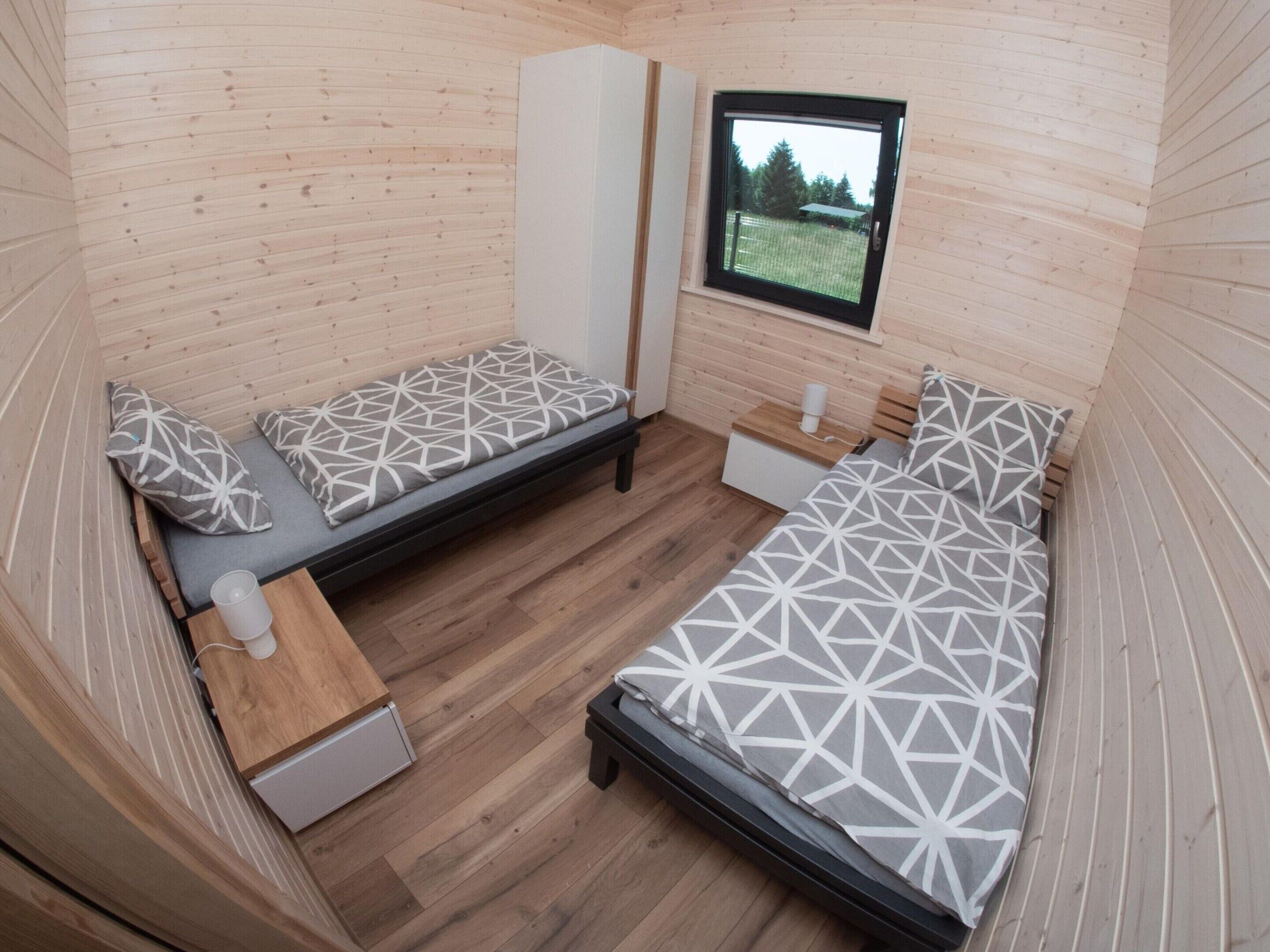 Ein kleines Zimmer mit zwei Betten, einem Fenster und einem Tisch mit einer Tasse.