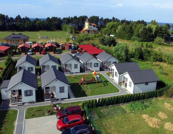 A residential area with multiple single-story houses, a playground, and a church in the background. - Holiday Homes Close to the Seaside Beach (Mielno)