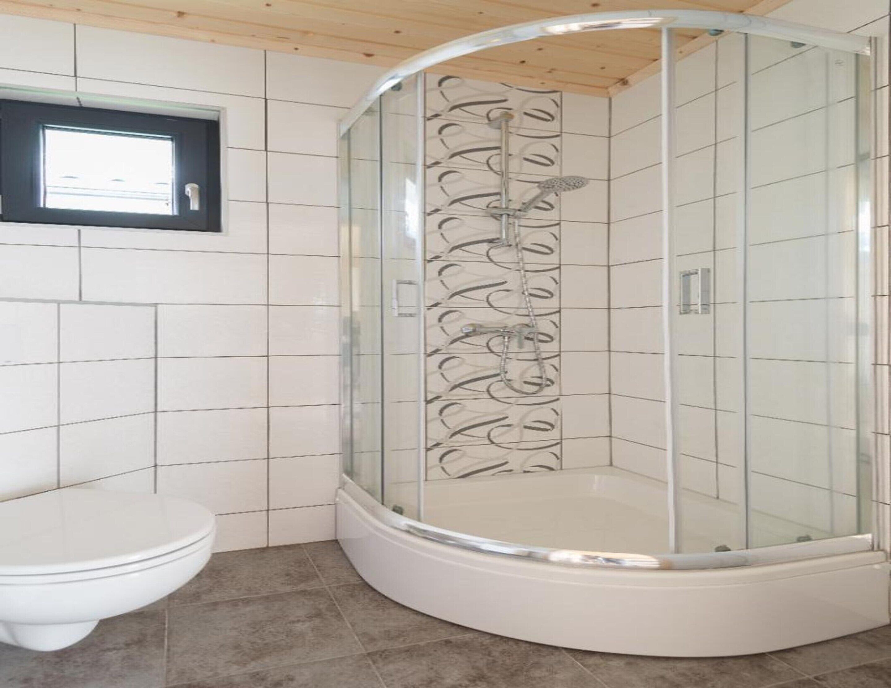 Ein Badezimmer mit einer gläsernen Duschkabine, einer weißen Toilette und Fliesenwänden.
