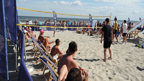 En strandvolleybollmatch med åskådare och spelare på sanden.
