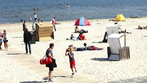 Una playa con gente tomando el sol, una tienda de campaña y un puesto de salvavidas.