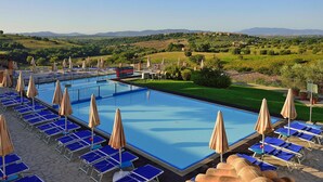 A rectangular swimming pool with blue lounge chairs and beige umbrellas arranged around it. - Apartment in Residence Borgo Magliano, in Magliano (Magliano in Toscana)