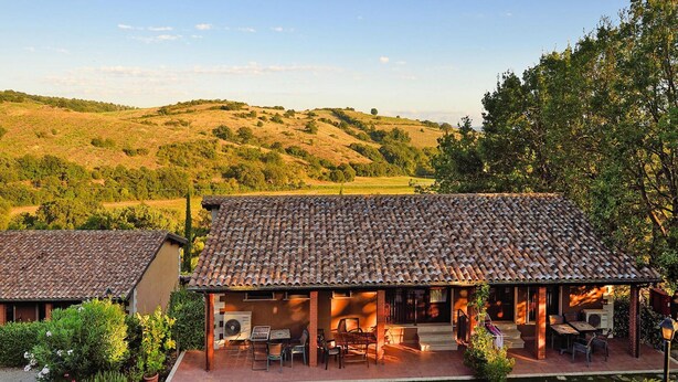 A villa with a tiled roof, outdoor seating area, and a garden. - Apartment in Residence Borgo Magliano, in Magliano (Magliano in Toscana)