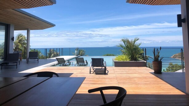 Een houten terras met lounge stoelen en een zwembad, met uitzicht op een schilderachtig zeegezicht.