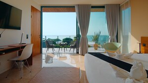 Een moderne hotelkamer met een groot bed, een bureau en een balkon met uitzicht op zee.