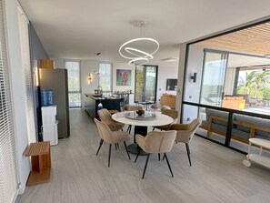 A modern kitchen with a central island, a dining area with round tables and chairs, and large windows offering views of the outdoors. - STUNNING sea views - LUXURY villa - INFINITY pool (Koh Phangan)