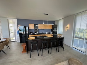 A modern kitchen with a central island, bar stools, and a dining area with a table and chairs. - STUNNING sea views - LUXURY villa - INFINITY pool (Koh Phangan)