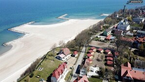 An aerial view of a coastal area with a beach, residential buildings, and a pier. - Spacious 3-room Apartment, Summer Pool (Postomino)