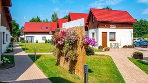 A row of wooden houses with red roofs, a paved walkway, and flower boxes. - Spacious 3-room Apartment, Summer Pool (Postomino)