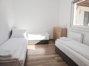 Une petite chambre propre, avec deux lits simples, une armoire en bois et une fenêtre.