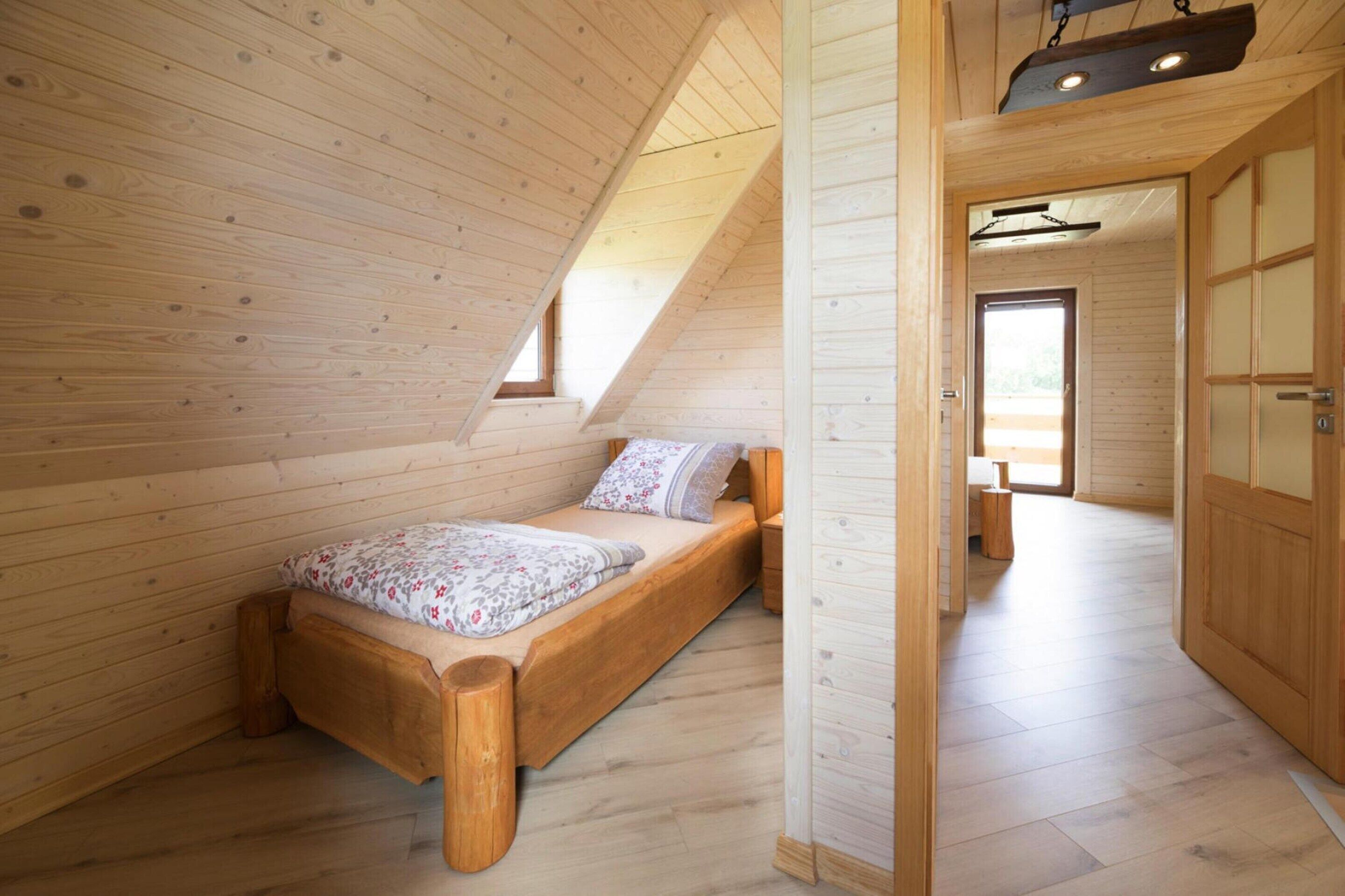 Een houten interieur met een schuine kap, een bed met bloemenbedrukking en een houten garderobe.