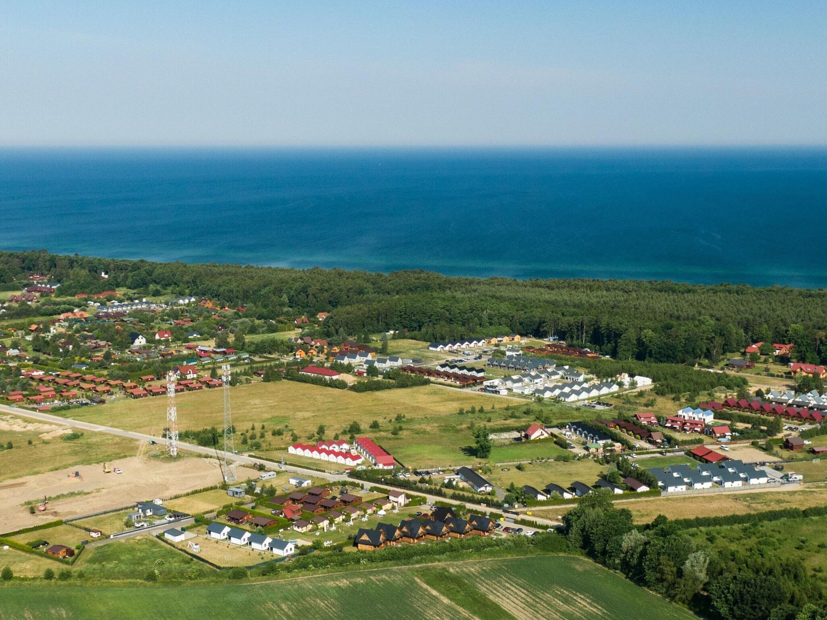 Luftaufnahme eines Küstdorfes mit Häusern, einem Strommasten und freiem Blick auf das Meer.