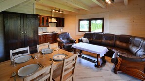 Un interior de cabaña acogedor, con zona de comedor, sofá de cuero, armarios de madera y un ventanal grande.