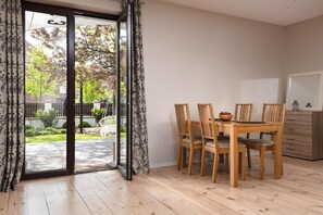 Un comedor con mesa y sillas, un armario de madera y un gran ventanal corredizo que da a un jardín.