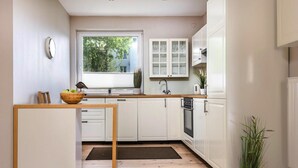A modern kitchen with white cabinets, a wooden island, a window, and a potted plant. - Apartment in Leba for Nature Lovers (Leba)