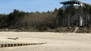 A modern building with a flat roof and large windows, surrounded by a forested area and a sandy beach. - Apartment in Pobierowo Near Beach and SPA (Rewal)