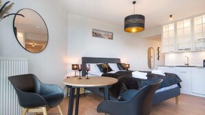 A modern bedroom with a bed, bedside tables, and a dining area with chairs and a table. - Apartment in Pobierowo Near Beach and SPA (Rewal)