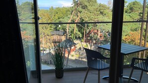A balcony with a view of a forested area, a table, and two chairs. - Apartment in Pobierowo Near Beach and SPA (Rewal)