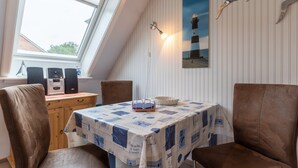 Ein Essbereich mit Tisch, der mit einer Tischdecke im Seestil bedeckt ist, zwei Stühlen, einem Radio und einer Wandleuchte.