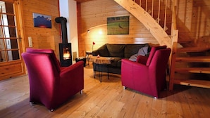Un interior de madera con chimenea, dos sillones rojos, un sofá y una escalera.