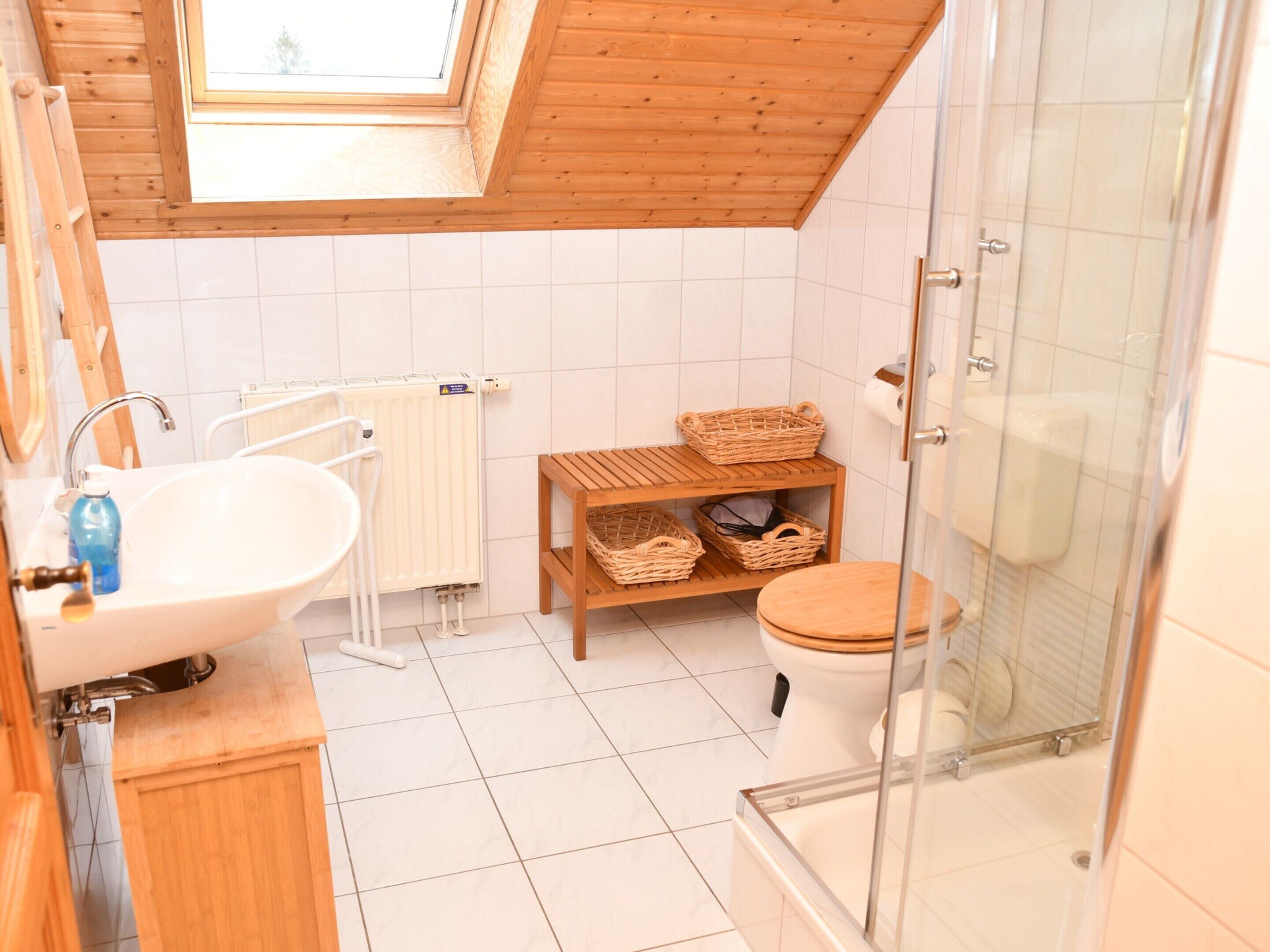 A modern bathroom with a skylight, a white sink, a wooden toilet, and a glass shower enclosure.