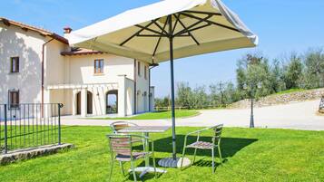 A patio with a table and chairs, a white umbrella, and a building with a tiled roof.