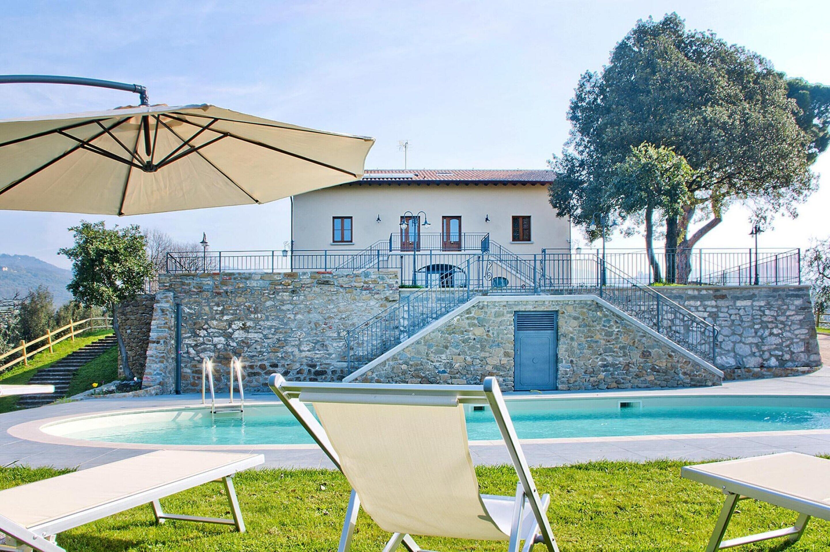 Zona de piscina con sillones, un muro de piedra y un edificio con balcón.