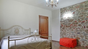 A bedroom with a metal bed frame, a wooden door, a stone wall, and a red bench. - Beautiful Apartment in Lamporecchio (Lamporecchio)