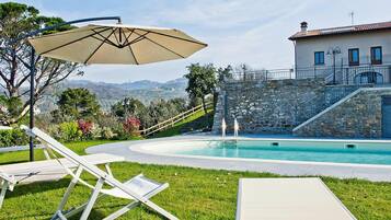 A poolside area with lounge chairs, an umbrella, and a stone staircase leading to a building.