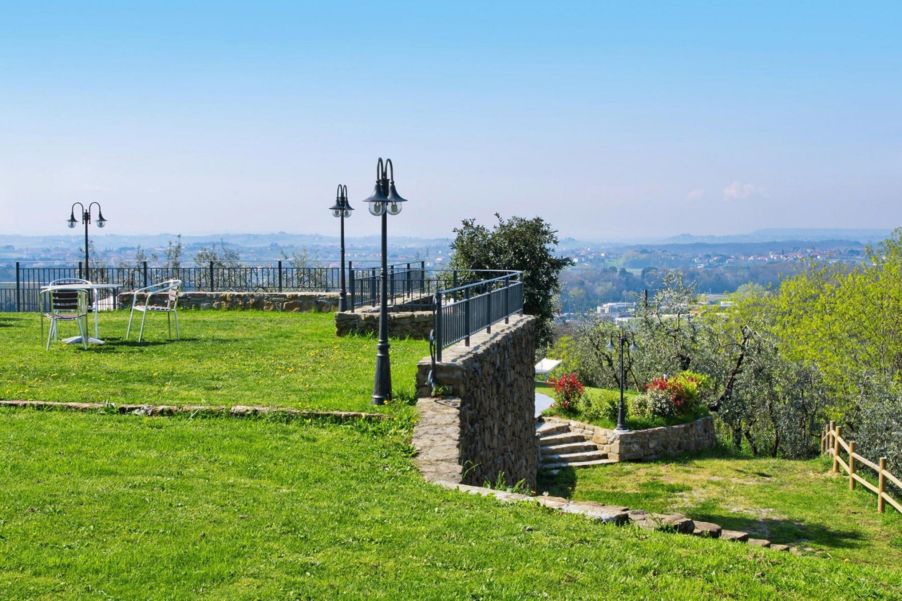 Une zone herbeuse avec des marches en pierre, des garde-corps en métal et des bancs.