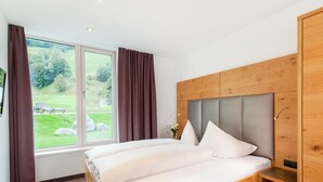 Un dormitorio con estructura de cama de madera, cabecera, ventana con cortinas y vista a un área verde.