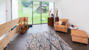 Amplia habitación con un gran ventanal corredero que da a un jardín, un banco de madera, un alfombra estampado y un sofá.