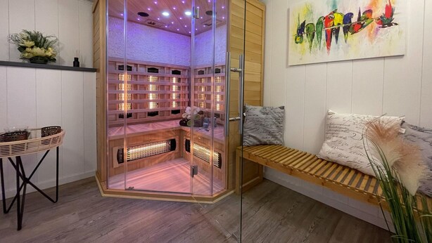 A modern room with a glass-enclosed sauna, a wooden bench, and a colorful abstract painting on the wall. - Holiday Home in Walkenried With Sauna (Walkenried)