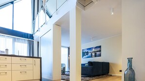 A spacious living area with a high ceiling, a modern kitchen, and a large window providing natural light. - Appartements im Maremuritz Yachthafen Resort (Waren (Müritz))