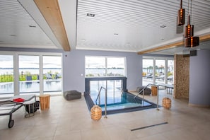 Un espace piscine intérieur moderne avec vue sur l’extérieur, un vestiaire et un comptoir d’accueil.