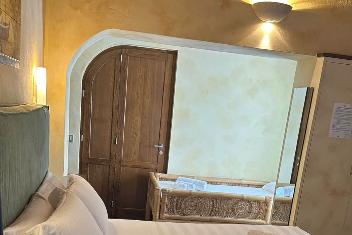 A single bed with white linens, a wooden wardrobe, and a small bedside table.
