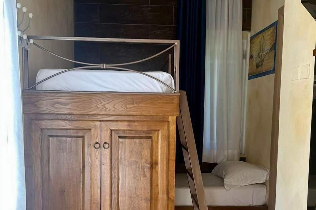A compact room with a bunk bed, wooden wardrobe, and a small seating area.
