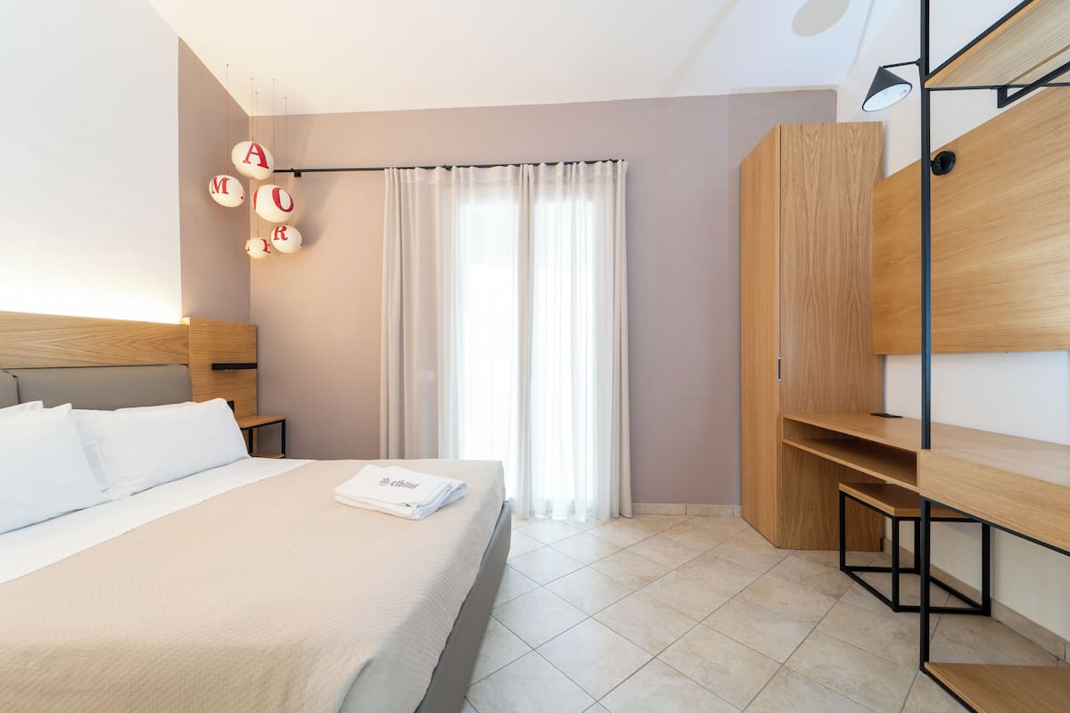 A modern hotel room with a neatly made bed, a wooden wardrobe, and a desk.