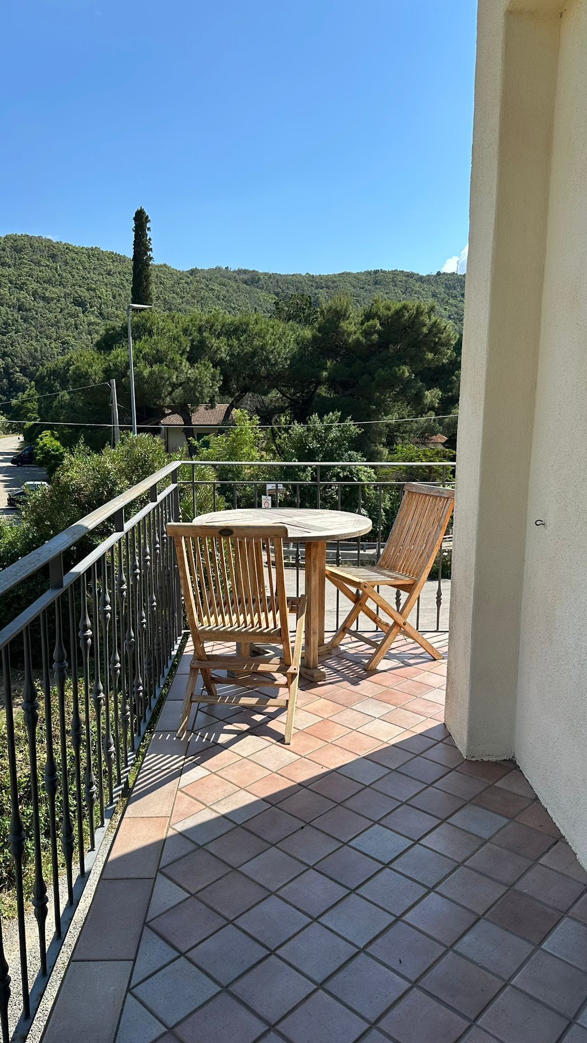 Ein Balkon mit einem runden Tisch und zwei Holzstühlen, mit Blick auf einen grünen Hügel.
