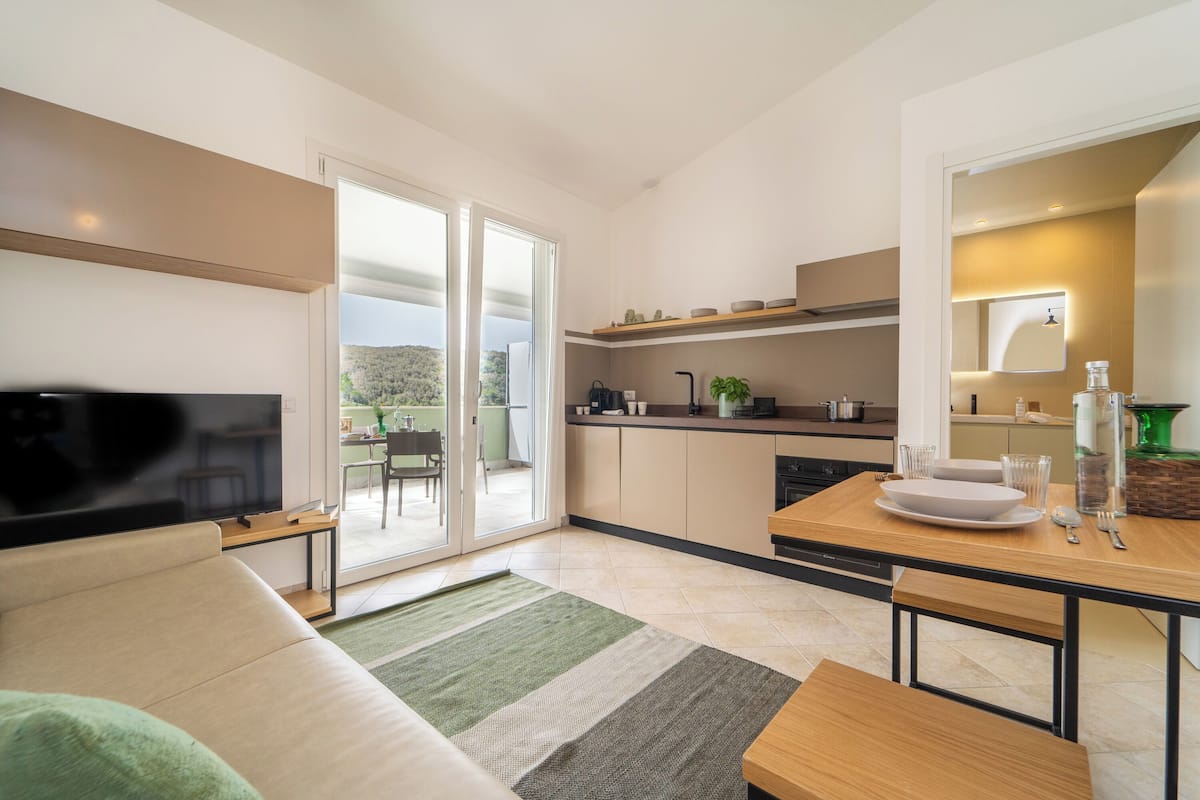 A modern living room with a flat-screen TV, a sofa, and a dining area with a table and chairs.