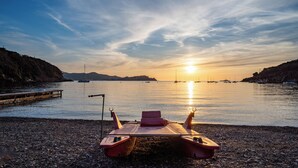 En träbåt på en stenstrand med en solnedgång i bakgrunden.