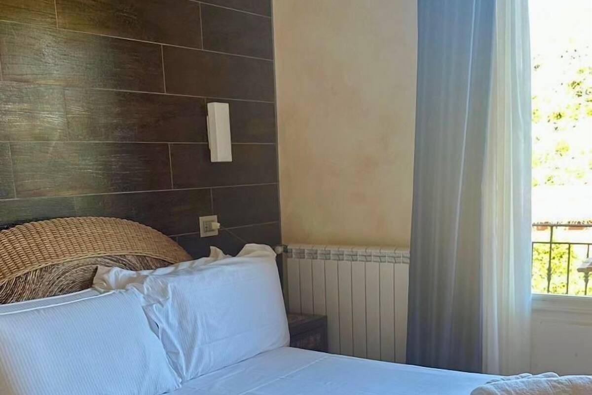 A neatly made bed with white linens and rolled towels, a dark wooden headboard, and a window with curtains.