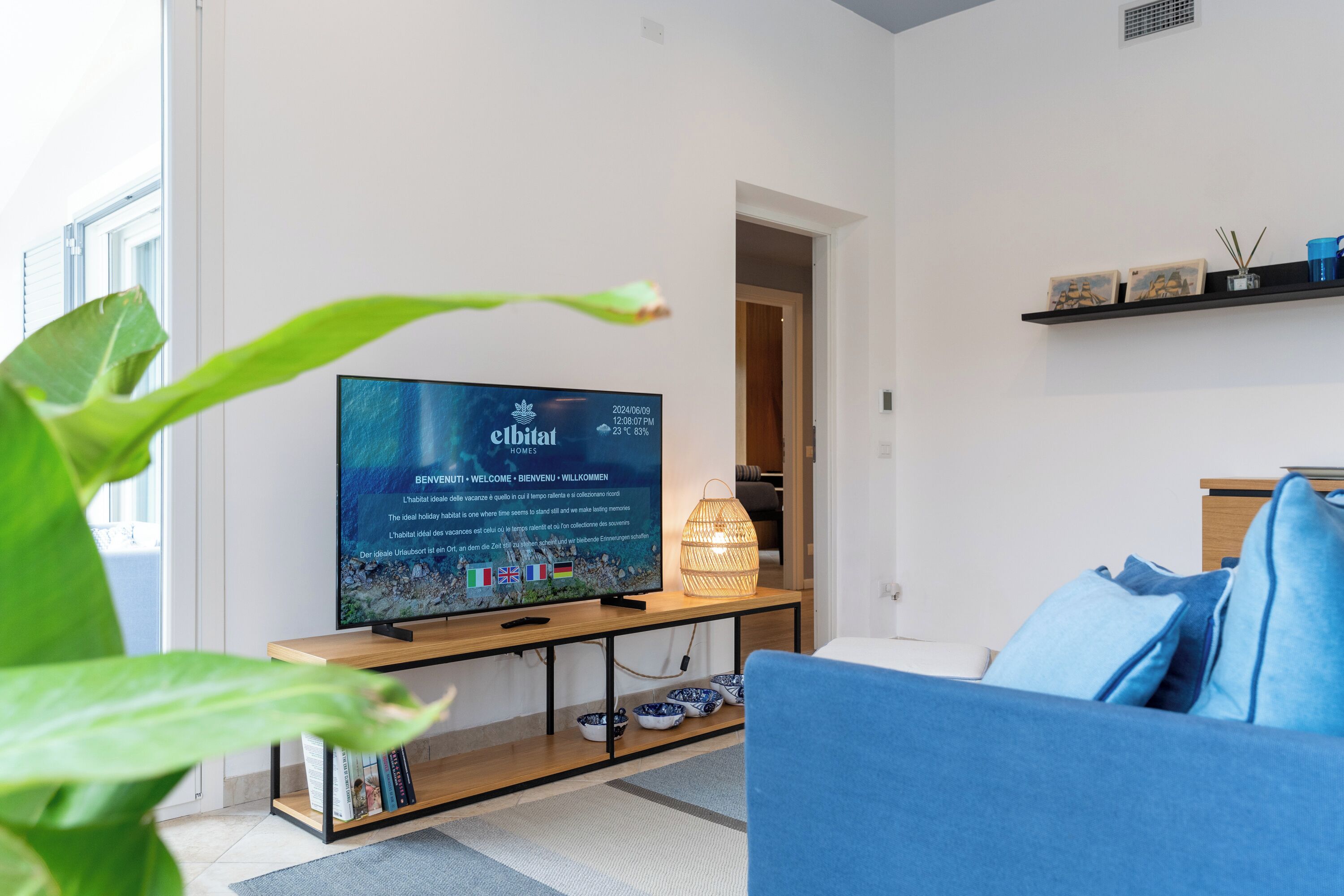 Una sala de estar moderna con un televisor de pantalla plana sobre un soporte de madera, un sofá azul y un estante pequeño con adornos.