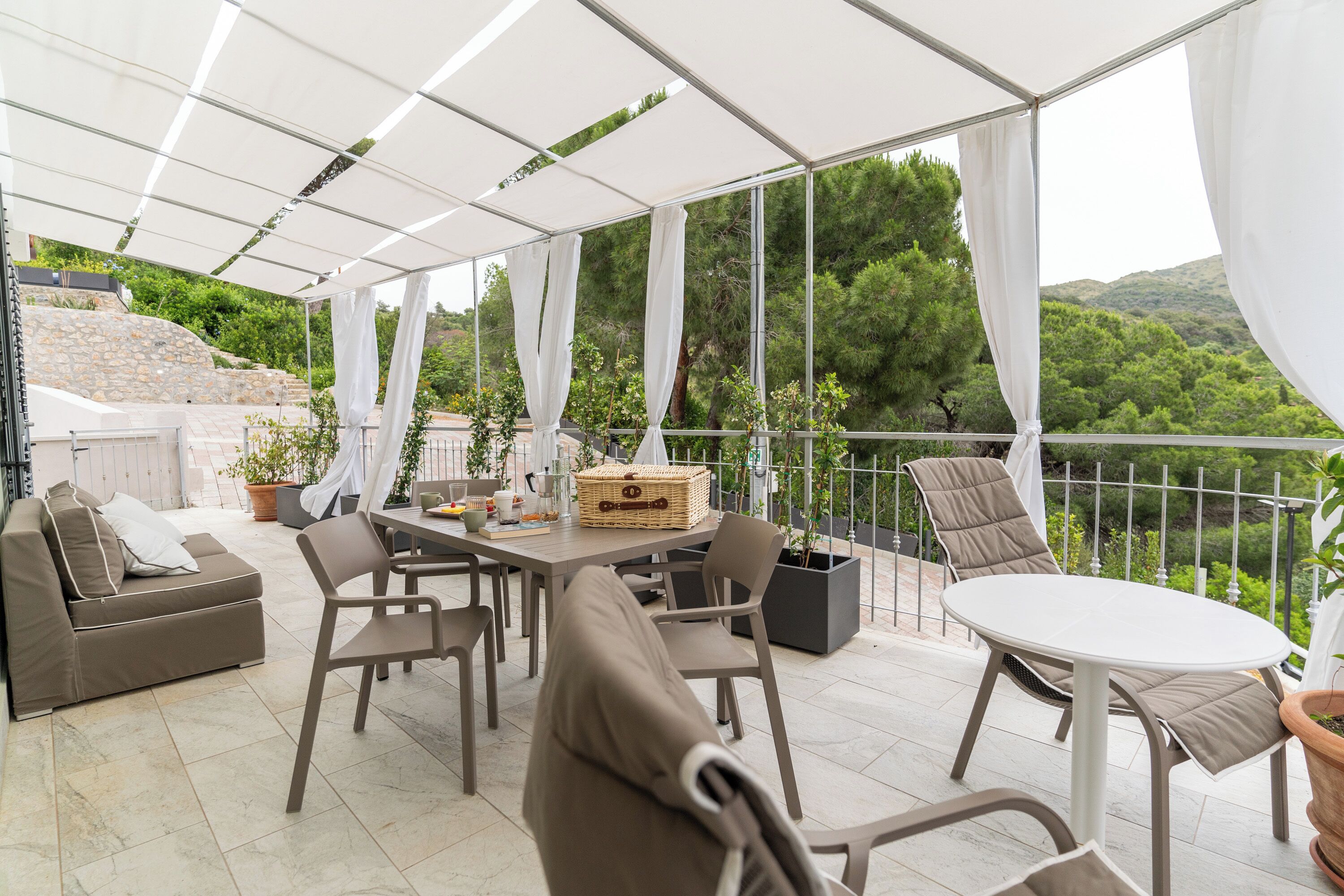 An outdoor patio with a table, chairs, a sofa, and potted plants.