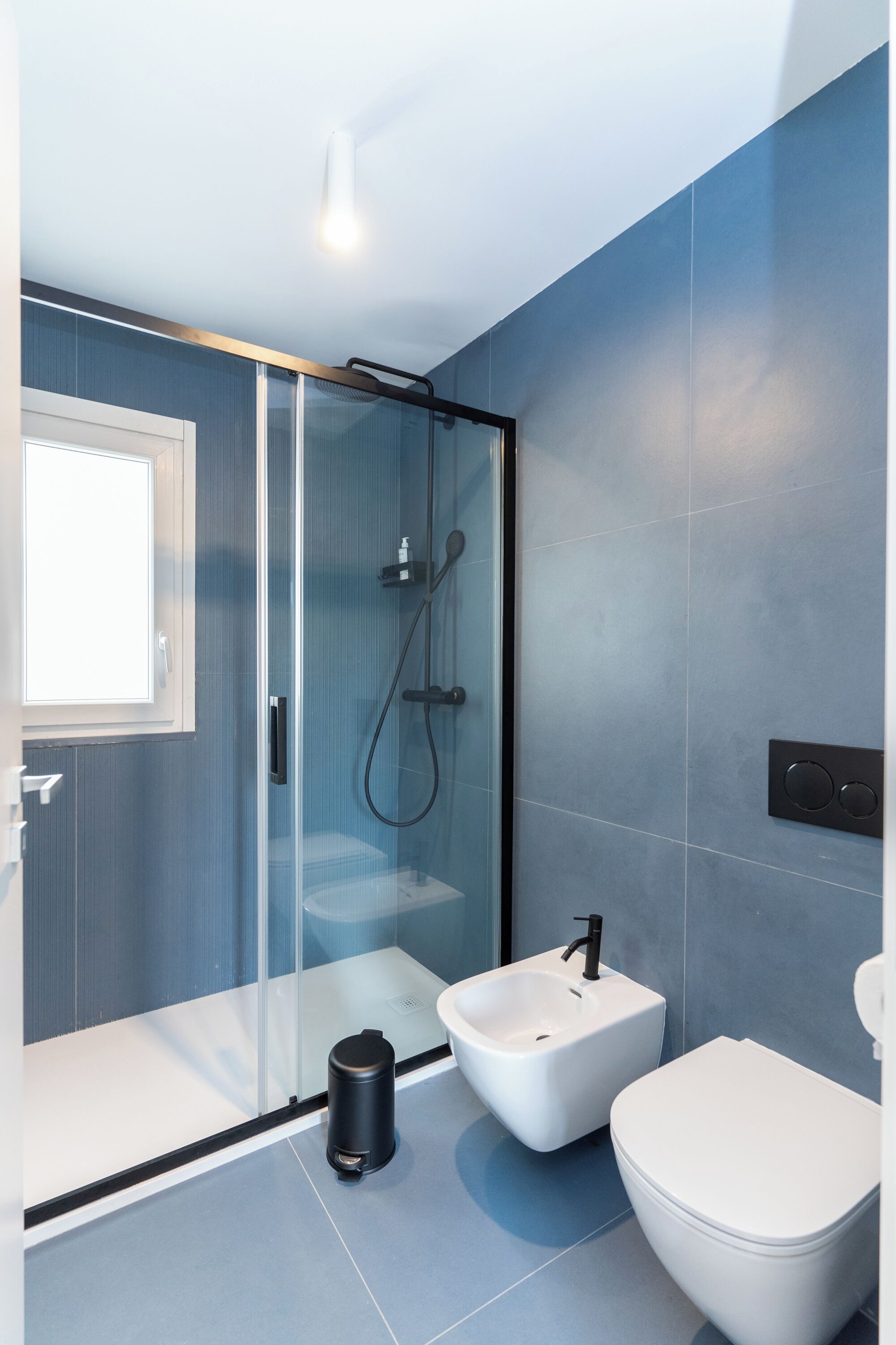 A modern bathroom with a glass-enclosed shower, a bidet, and a toilet.