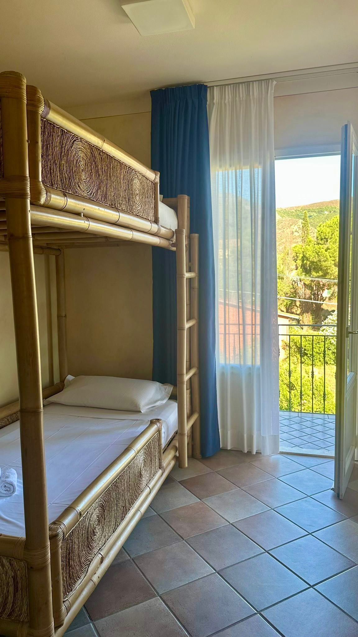Une chambre avec des lits superposés donnant sur un balcon et sur la verdure environnante.