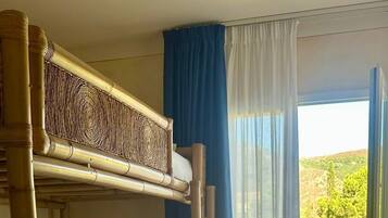 Une chambre avec des lits superposés donnant sur un balcon et sur la verdure environnante.